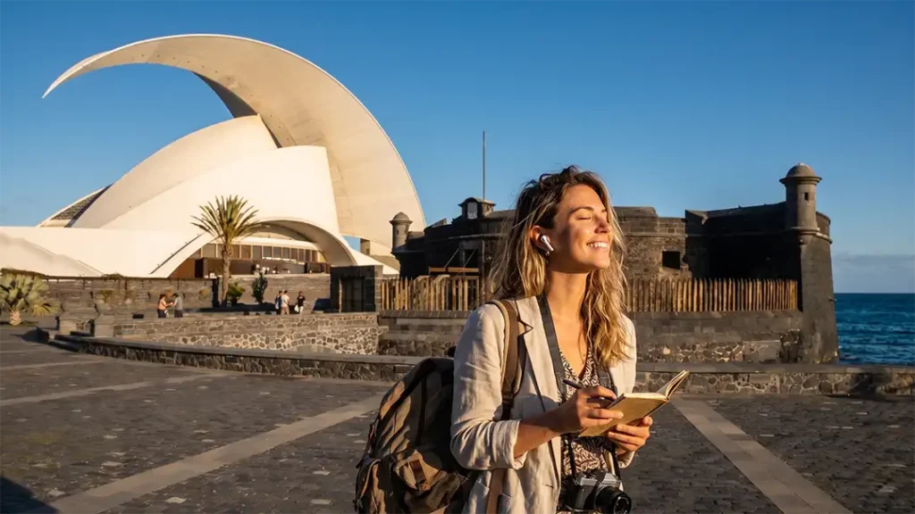 Une femme vit une expérience audio immersive à Santa Cruz de Tenerife, avec l'Auditorium et le Castillo Negro en arrière-plan.