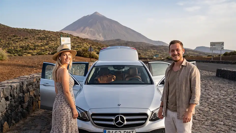 Ein Reisepaar lauscht neben seinem Auto im Nationalpark Las Cañadas einem Audioguide mit dem Teide im Hintergrund.